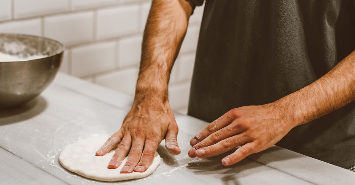 Food cost pizzeria — il pizzaiolo pesa i panetti di impasto su una bilancia